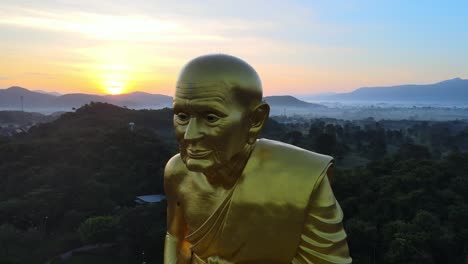 4k aerial close up shot of a biggest luang pu thuat statue in the world surrounded by mountains of khao yai at dawn in thailand