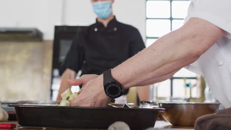 cocinera caucásica que enseña a un grupo diverso usando máscaras faciales