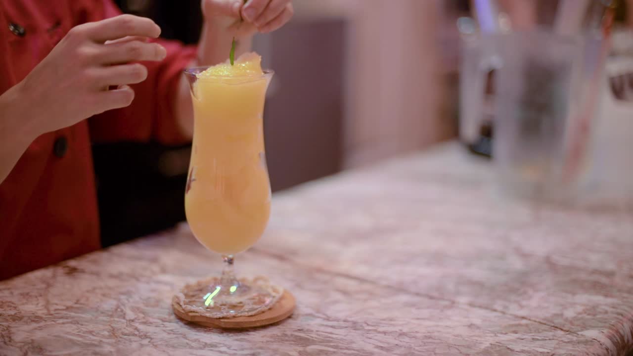Barman barista bartender decorating an orange smoothie a cocktail glass with some mint leafs at a local cafe diner restaurant in Mexico latin america