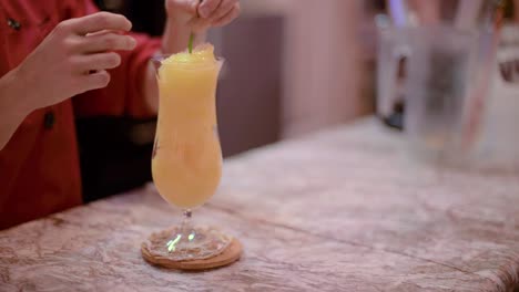barman barista bartender decorating an orange smoothie a cocktail glass with some mint leafs at a local cafe diner restaurant in mexico latin america