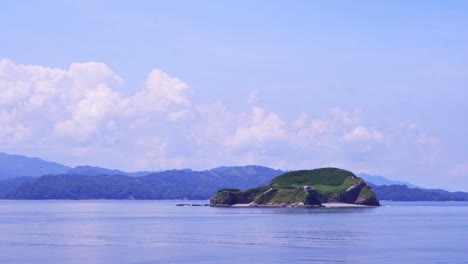 passing island with mountains on the horizon in costa rican landscape on sunny day with cloudy sky, full shot