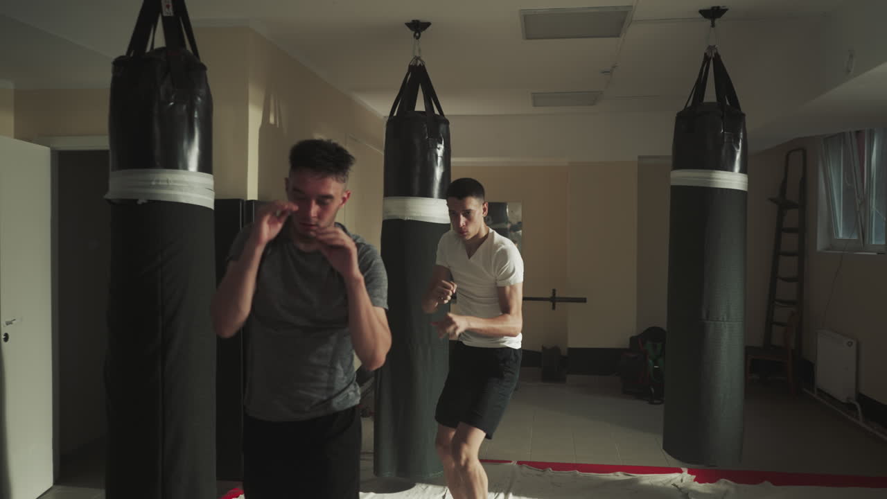 남자 권투 선수 그룹은 권투를 연습하는 동안 코치를 따라 치 운동을 반복합니다. 활발한 움직임을 통해 근육을 구축합니다. 체육관에서 리더의 지침