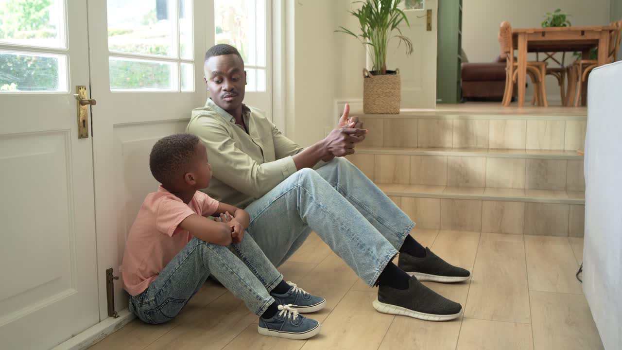 African American father and son sitting by glass door, father ruffling hair, hugging, comforting