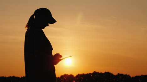 Silueta-De-Una-Mujer-Campesina-Que-Trabaja-Con-Una-Tableta-En-La-Vista-Lateral-Al-Atardecer