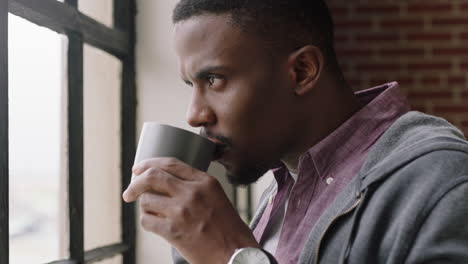 portrait young african american man drinking coffee at home enjoying relaxed morning looking out window planning ahead thinking successful male relaxing close up