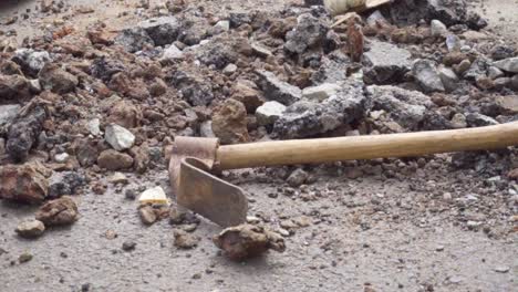 rusty old digging tool shaped like a pickaxe with a forged adze isolated against a rock and tar debris, slow motion pan