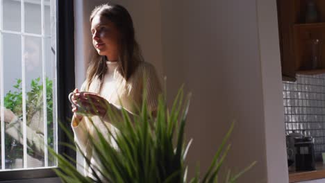 woman with coffee cup looking out of window at home