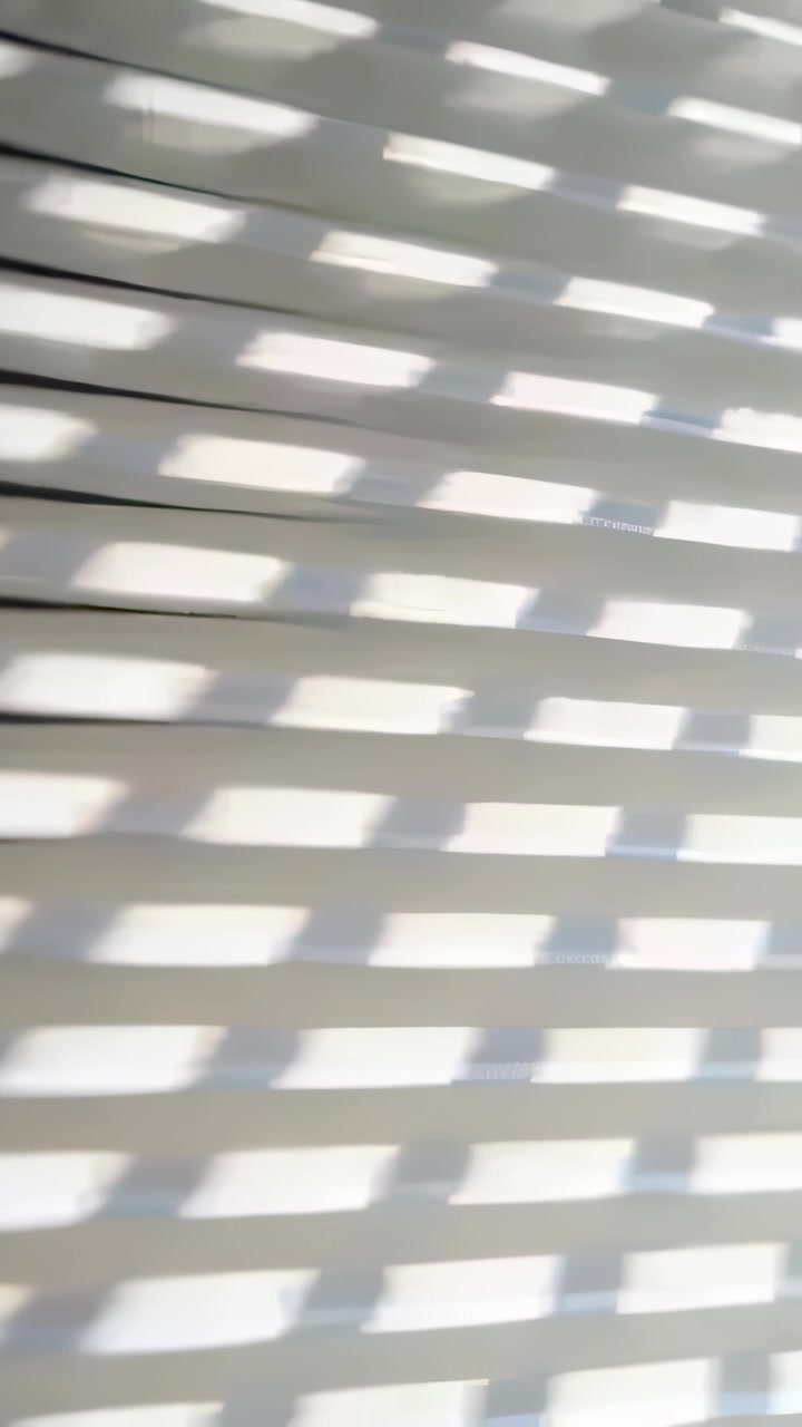 Vertical video: Casting light through slatted blinds at window shifting patches down, sun drifting