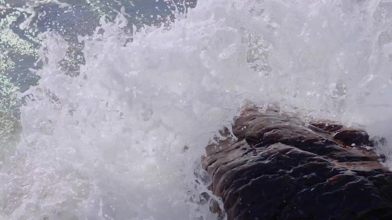 Una ola rompe contra una roca rociando espuma en el aire