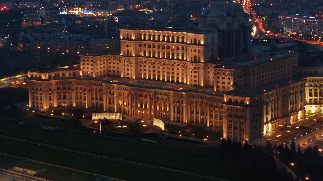 Aerial drone view of illuminated Palace of the Parliament in Bucharest downtown in the evening. Multiple districts around. Romania