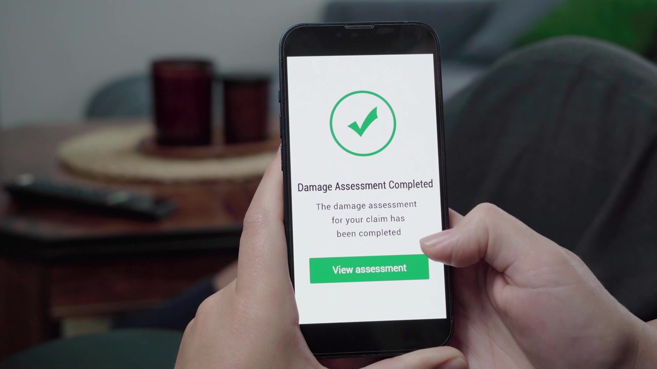 Primo piano di una persona che controlla una schermata di conferma del completamento della valutazione del danno di un sinistro su un'app di assicurazione digitale