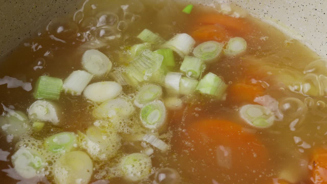 Nærbillede, tilføjelse af hakket porre til kogende vegetarisk suppe, simrende suppe