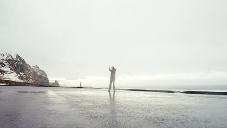 Silhouette-of-Lonely-Man-by-Icelandic-Coastline-Taking-Picture-With-Smartphone-on-Cold-Rainy-Day,-Cinematic-Low-Angle-Approaching