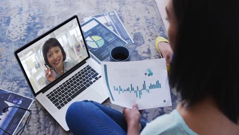 African-american-woman-holding-a-document-having-a-video-call-with-female-colleague-on-laptop