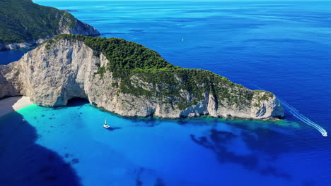 Navagio-Beach,-Greece-with-the-remains-of-a-shipwreck-on-the-sand-in-the-cove---panning-aerial-reveal