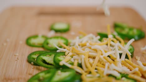 queso rallado multicolor cayendo sobre jalapeños en rodajas verdes brillantes en una tabla de cortar en cámara lenta