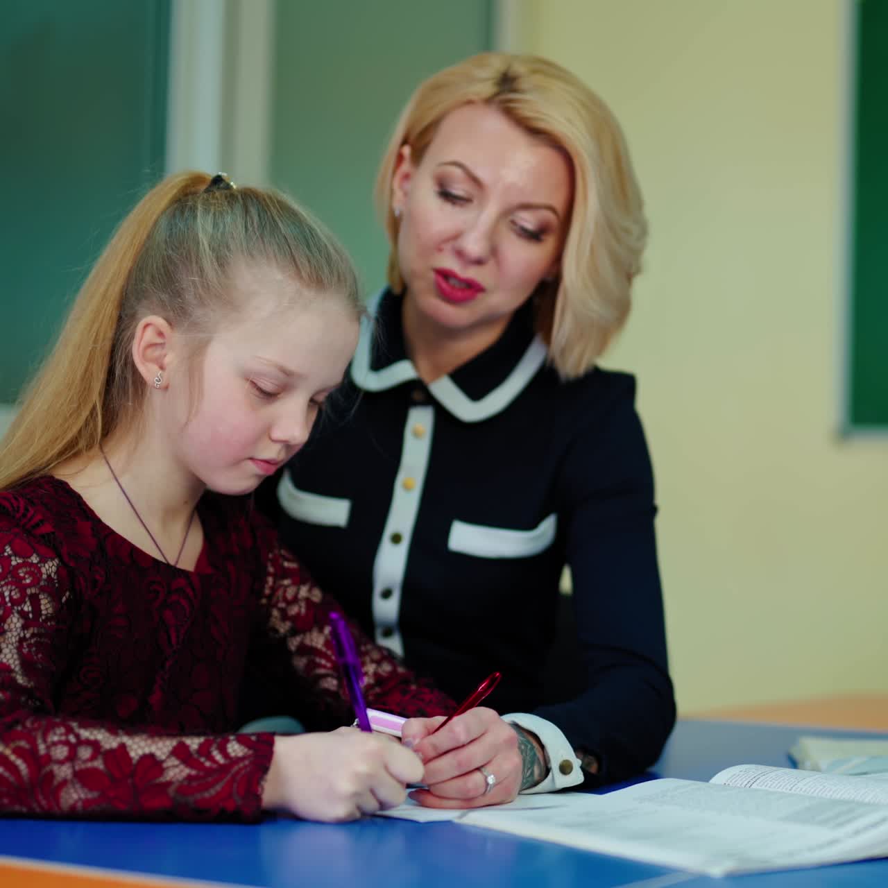 Caring teacher with a pupil. Woman tutor helping school child girl studying. Primary schoolgirl learning writing in notebook with the help of female educator at school.