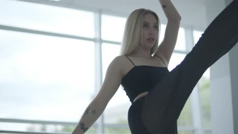 fit girl in black clothes performing contemporary. female dancer shows flowing motions, body and hands waves at white room. modern ballet dance choreography. young woman is moving smoothly