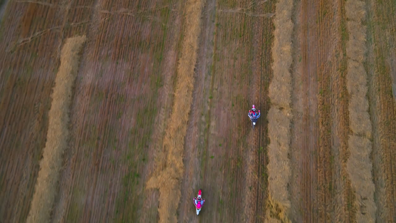 Riding motorbikes in the field with left hay. Happy couple of young people riding their vehicles in the cut farmlands. Bird's eye view.
