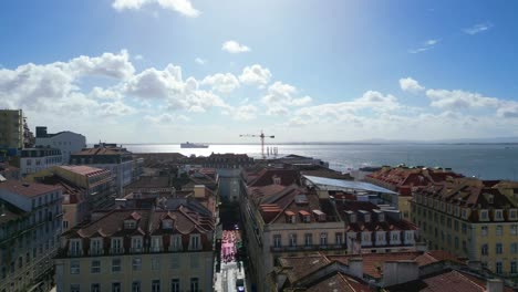 Volando-Hacia-Atrás-Sobre-La-Calle-Rosa-Ubicada-En-Cais-Do-Sodre-En-La-Ciudad-De-Lisboa-Con-Gaviotas-Volando-Y-El-Río-Tejo-Como-Fondo-Y-Paisaje-Urbano-De-Lisboa,-Portugal