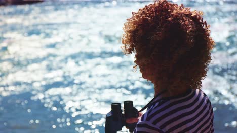 mujer con binoculares junto al agua