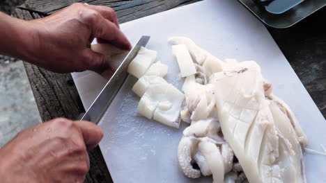 persona corta un filete de calamar con un cuchillo en anillos de calamar, tabla de cortar blanca