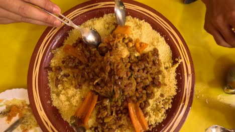 A-traditional-Arabic-Friday-lunch-as-intergenerational-hands-gather-around-a-big-couscous-plate-filled-with-flavorful-meat-and-vegetable-couscous,-a-festive-dish-rich-in-herbs-and-spices