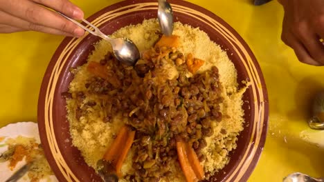 a traditional arabic friday lunch as intergenerational hands gather around a big couscous plate filled with flavorful meat and vegetable couscous, a festive dish rich in herbs and spices