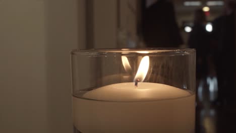 Tight-Shot-of-a-Burning-Candle-at-a-Wedding-Reception-with-Guests-in-Background