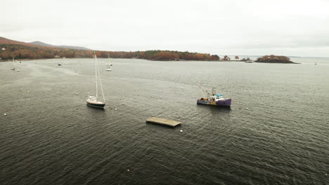 Hummerboot-Und-Segelboot-In-Der-Bucht-Verankert,-Nebliger-Herbsttag,-Drohnenaufnahme