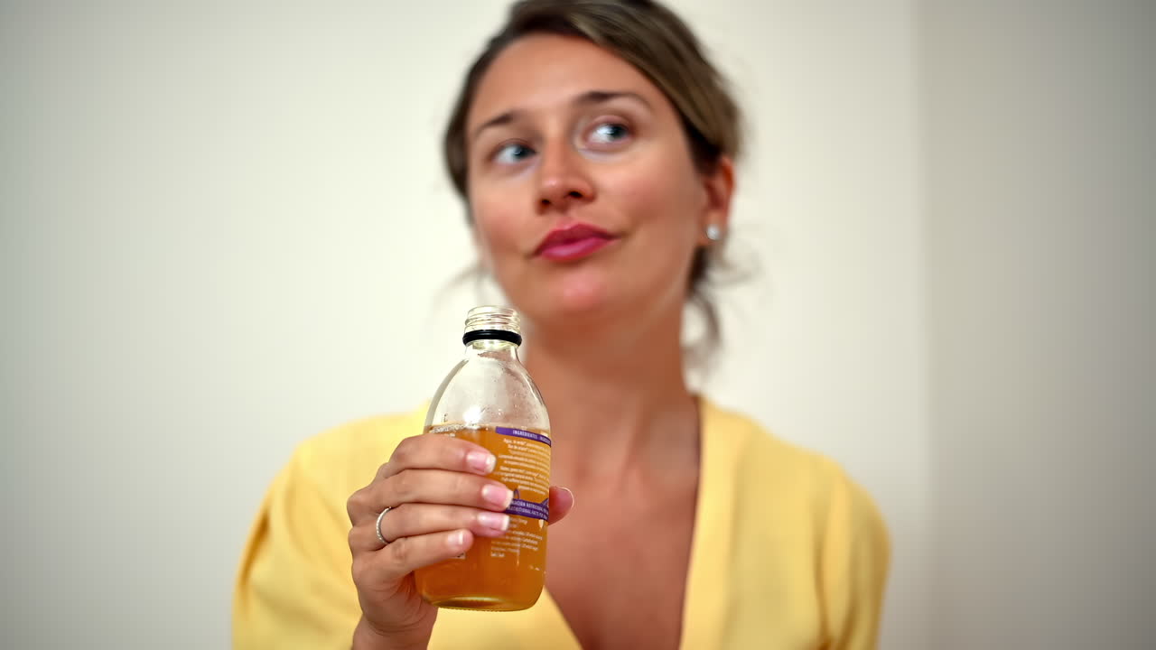 A woman in bright clothing takes a sip from a glass of juice while sitting comfortably in her home. The warm atmosphere adds to her relaxed mood and enjoyment