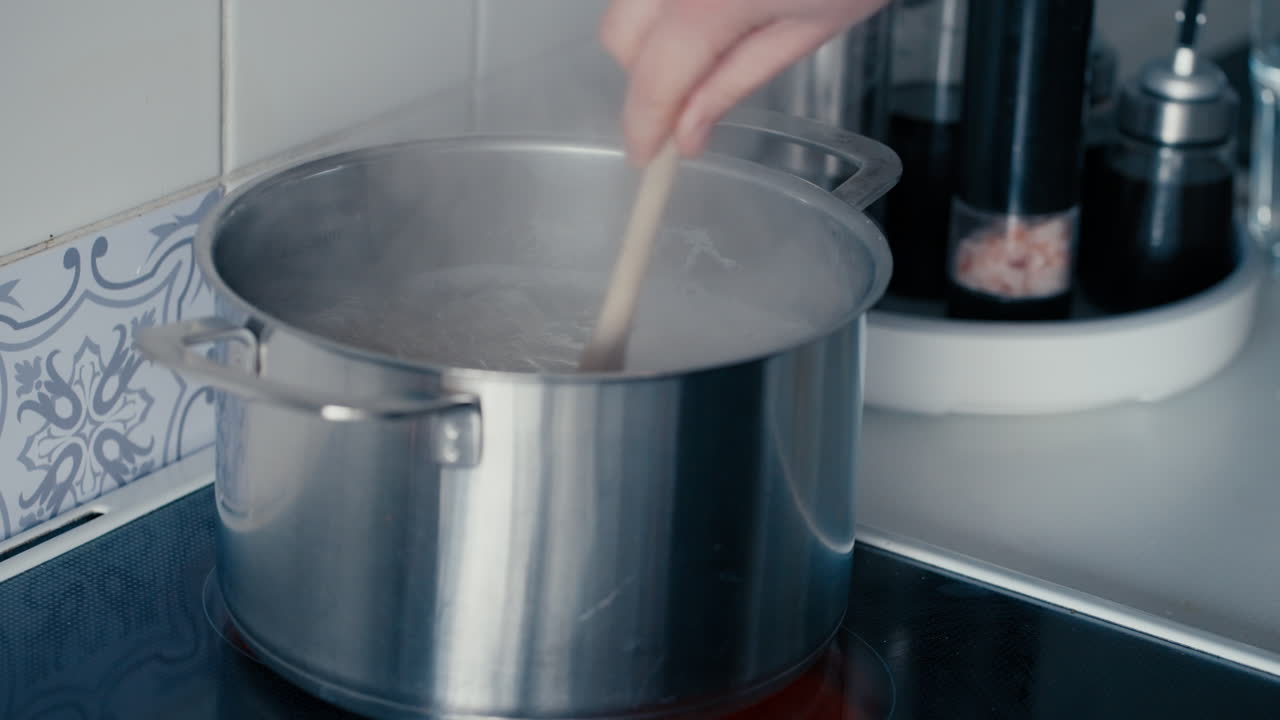 Primo piano di una donna che mescola gli spaghetti in acqua bollente al rallentatore, di giorno in cucina.