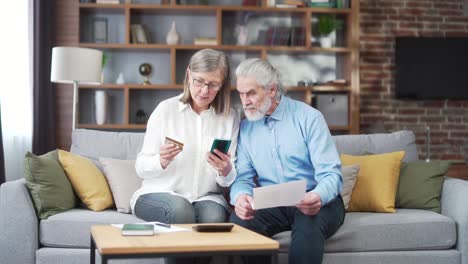 senior family couple, gray haired old man and woman pay for services enter data documents using application mobile smartphone