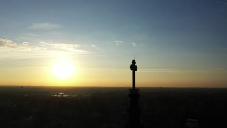 una toma aérea del campanario de una catedral con una cruz en la parte superior, tomada al amanecer