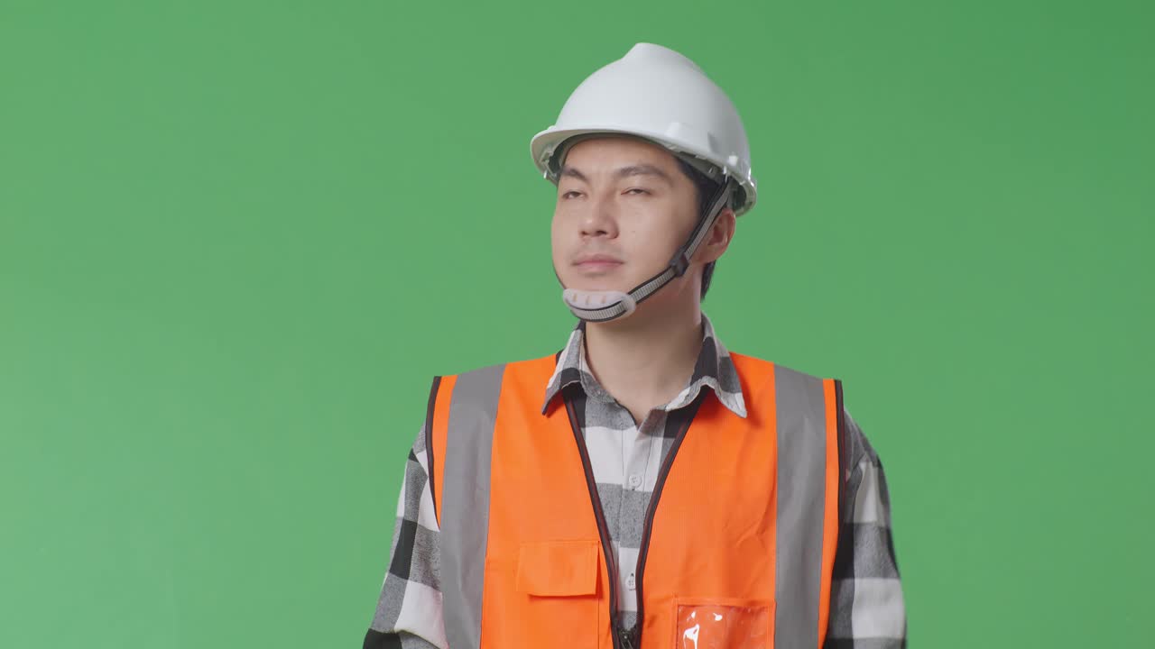 안전 헬을 입은 아시아 남성 엔지니어가 녹색 스크린 배경 스튜디오에서 는 동안 주변을 둘러보고 있습니다.