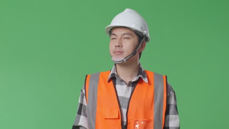 close up of asian male engineer with safety helmet looking around while walking in the green screen background studio