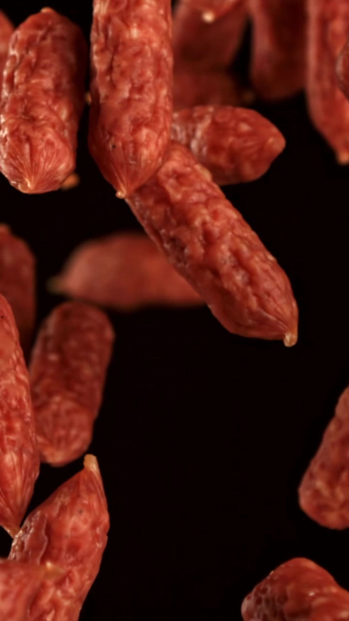 Mini salsicce di salame che cadono al rallentatore su sfondo nero.