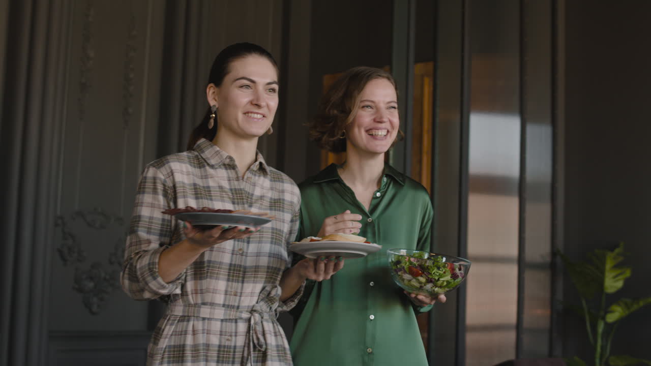 dos mujeres felices sirviendo comida en la mesa del comedor mientras tienen una reunión familiar en casa
