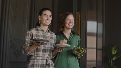 two happy women serving food at the dining table while having a family reunion at home