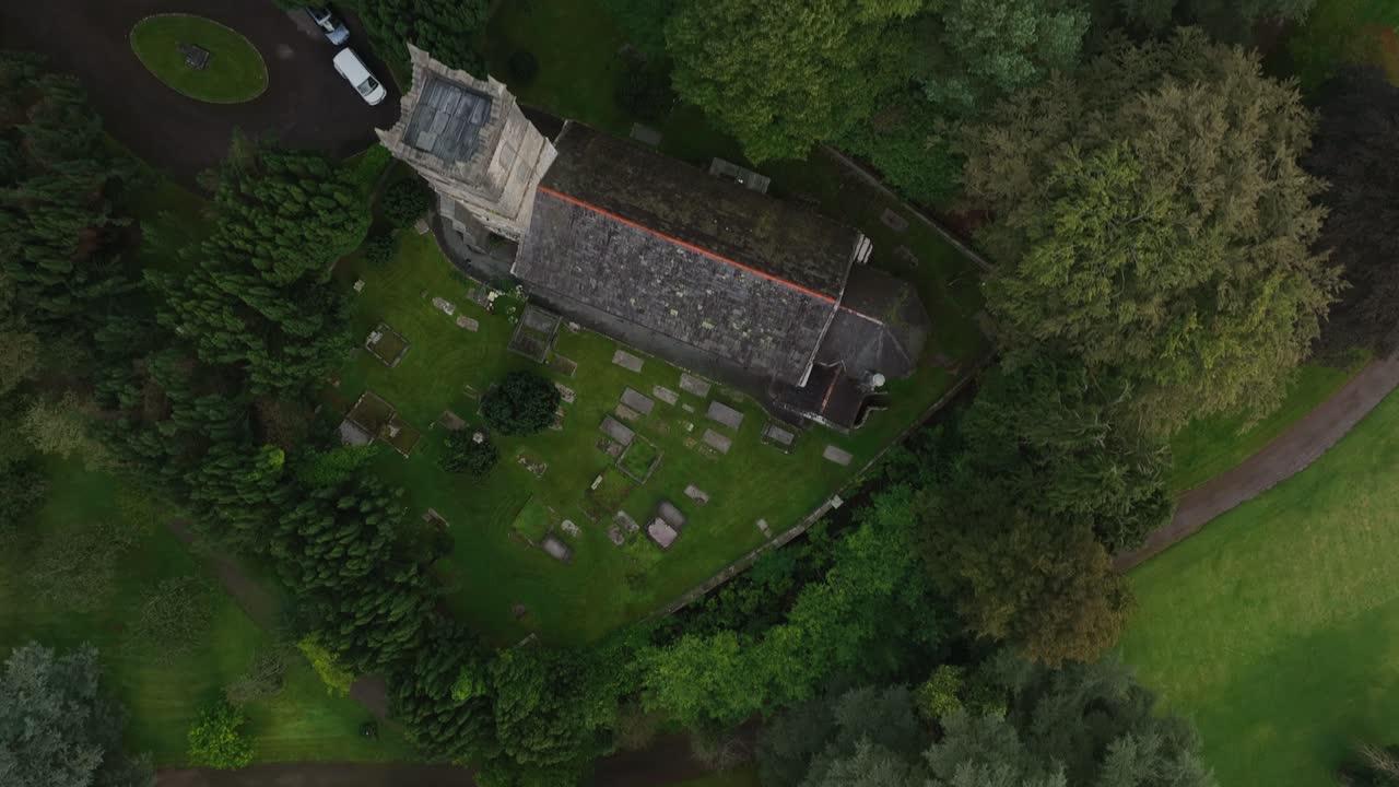 St. Salvator's Church, Glaslough, County Monaghan, Ireland, September 2022. Drone bird’s eye view top shot tracking forward over forest tree top canopy, graveyard and weathered church roof