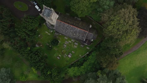 st. salvator's church, glaslough, county monaghan, ireland, september 2022. drone bird’s eye view top shot tracking forward over forest tree top canopy, graveyard and weathered church roof