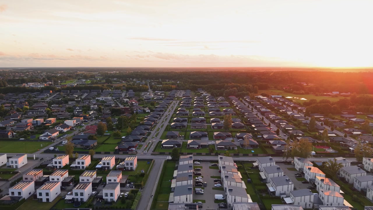 Imagens aéreas deslumbrantes de um espaçoso bairro suburbano moderno capturadas ao pôr do sol, exibindo fileiras de casas contemporâneas, ruas tranquilas e vegetação exuberante sob uma luz dourada e quente.