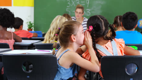 schoolgirl whispering into her friend s ear in classroom