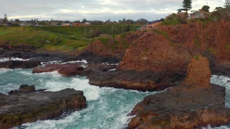 olas espumosas chocando contra los acantilados anaranjados y marrones en las rocas de la catedral cerca de la ciudad costera en kiama downs, nueva gales del sur, australia - toma aérea