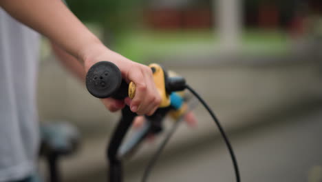 a close-up of a little boy's hand gripping the brake of a bicycle while wearing a white top, with a blur background view