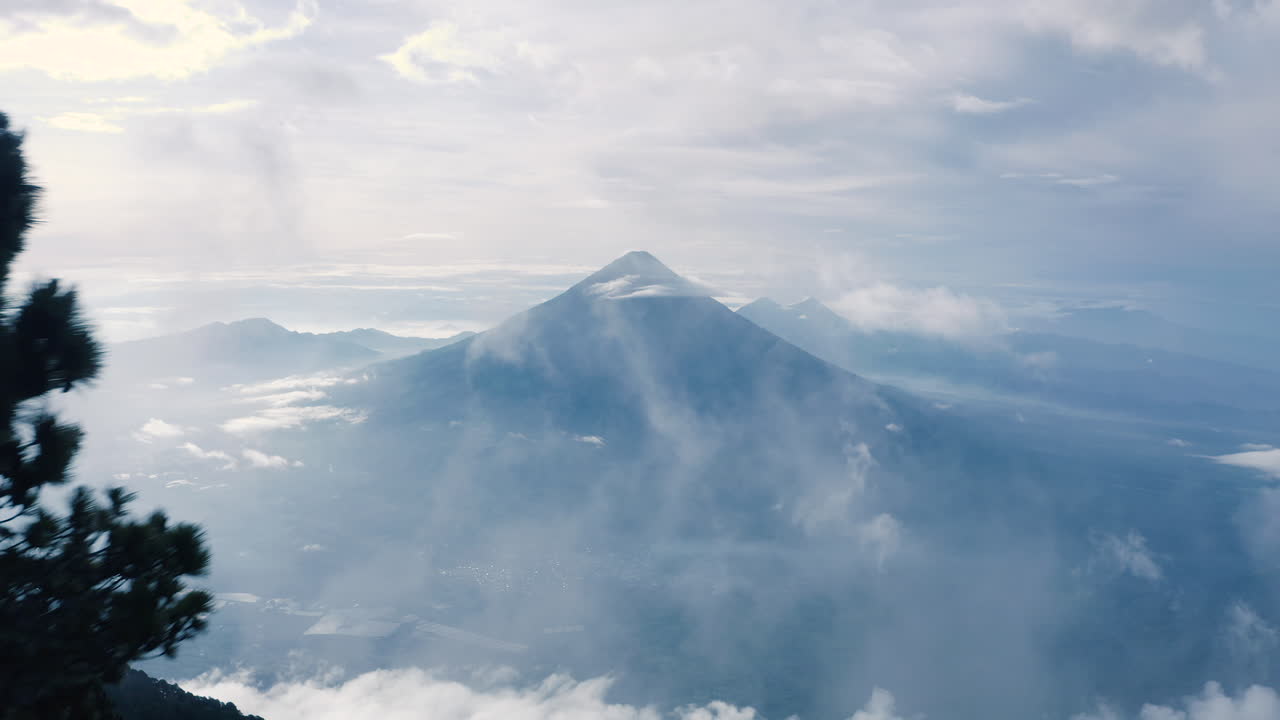 el dron vuela más allá de los árboles alpinos para revelar un hermoso volcán rodeado de nubes finas.