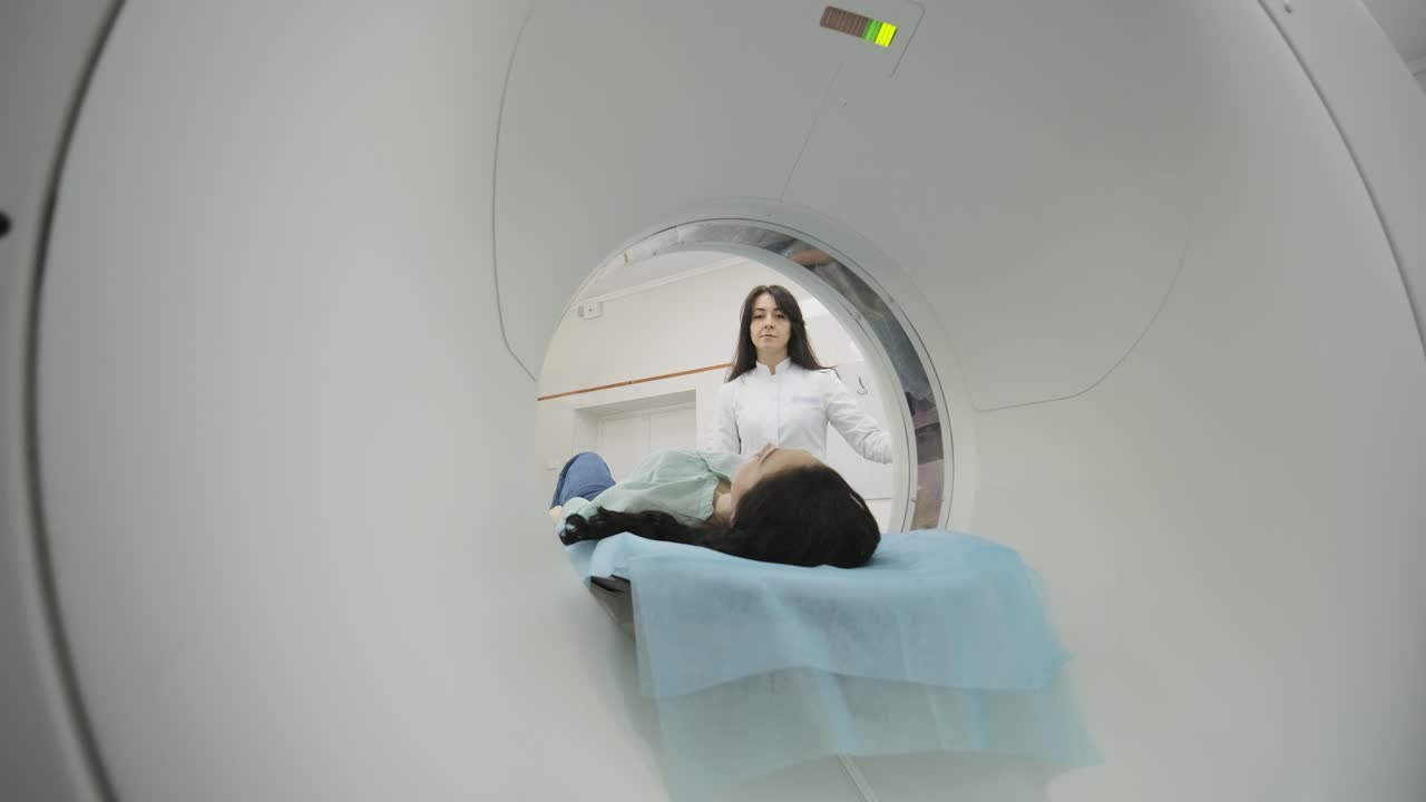 Female patient is undergoing CT or MRI scan under supervision of a radiologist in modern medical clinic. Patient lying on a CT or MRI scan bed, moving outside the machine.