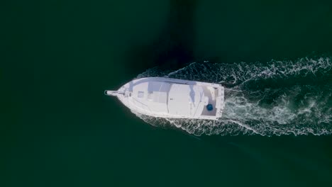 Birdseye-view-tracking-white-boat,-wake,-and-long-shadow-on-sunny-day