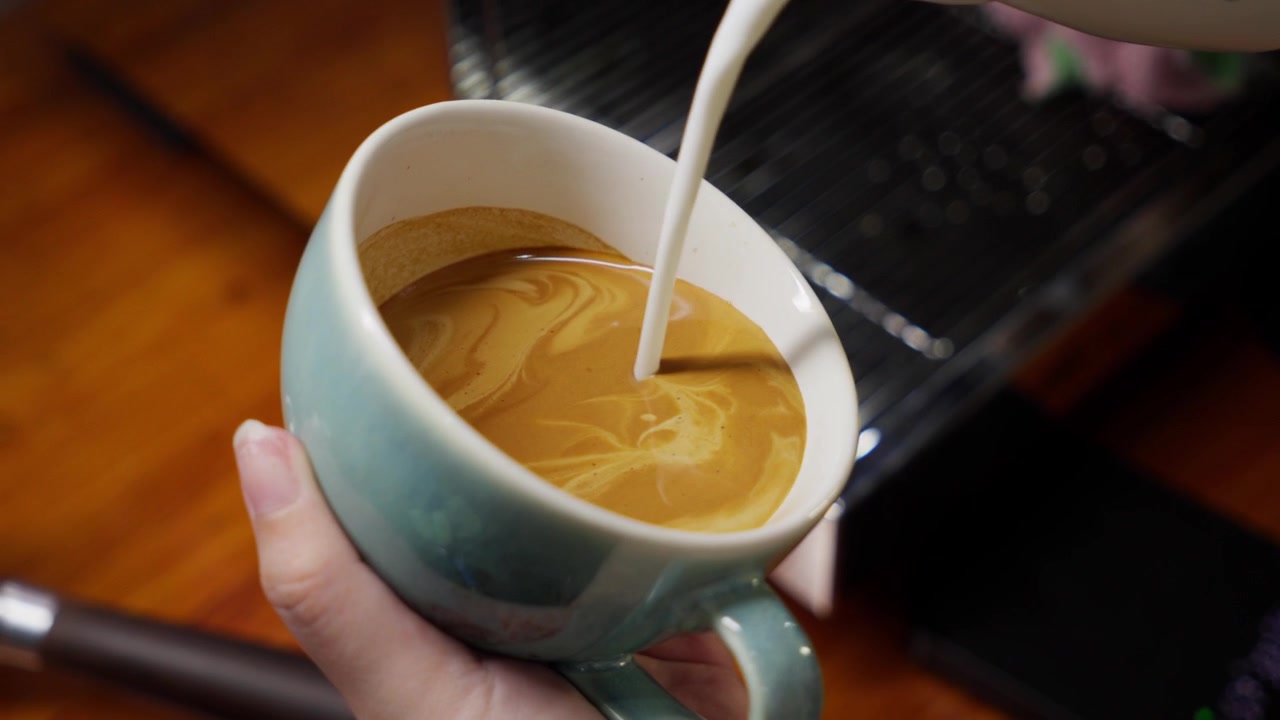 Mano del barista che realizza Latte Art in una tazza di caffè. Primo piano.