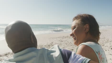 Sonriente-Pareja-Afroamericana-Senior-Abrazándose-Y-Mirando-El-Mar-En-La-Playa-Soleada
